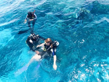 Üç dalgıçlardan siyah tüplü dalış takım elbise, bir adam ve bir kadın oksijen şişe ile lavabo şeffaf mavi su deniz, okyanus bir tropik cennet sıcak tatil altında.