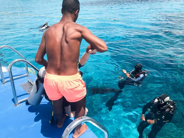 Dalgıçlar siyah tüplü dalış takım elbiseli oksijen şişeleri alıcıları şeffaf mavi su denizin altında ile bir siyah, yağız, Arap atletik atletizm adam yardım, bir tropik cennet okyanusta sıcak resort.