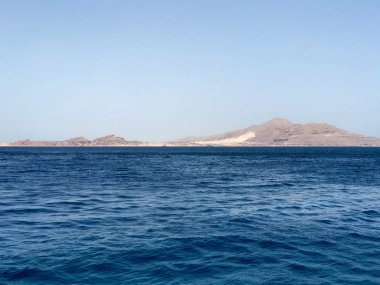 Sarı kum uzak taş dağlardaki tropik sahil beldesi mavi tuz deniz manzaralı güzel bir deniz manzarası.