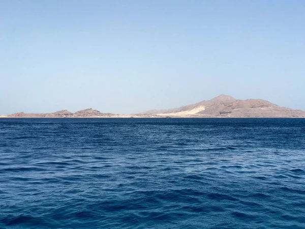 Sarı kum uzak taş dağlardaki tropik sahil beldesi mavi tuz deniz manzaralı güzel bir deniz manzarası.