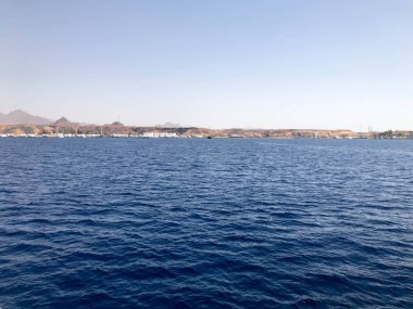 Uzak güzel tropikal kahverengi taş dağlar ve farklı evlerin Seascape, kıyı ve mavi tuz Azure deniz üzerinde binalar, mavi gökyüzüne karşı okyanus.