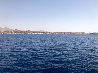 Uzak güzel tropikal kahverengi taş dağlar ve farklı evlerin Seascape, kıyı ve mavi tuz Azure deniz üzerinde binalar, mavi gökyüzüne karşı okyanus.