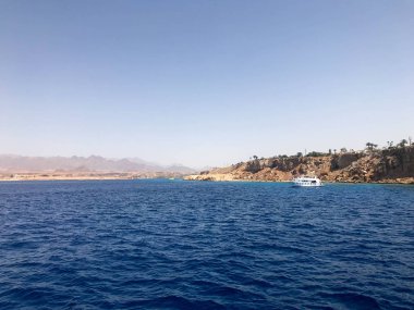 Uzak güzel tropikal kahverengi taş dağlar ve çeşitli binalar, sahildeki gemi ve mavi tuz Azure deniz, okyanus mavi gökyüzüne karşı deniz manzarası.