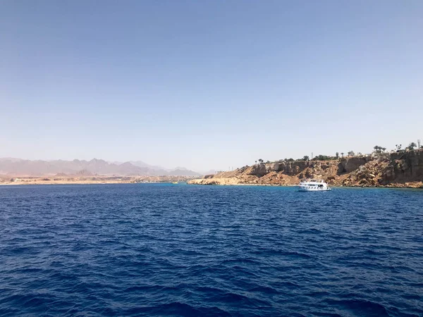 Uzak güzel tropikal kahverengi taş dağlar ve çeşitli binalar, sahildeki gemi ve mavi tuz Azure deniz, okyanus mavi gökyüzüne karşı deniz manzarası.