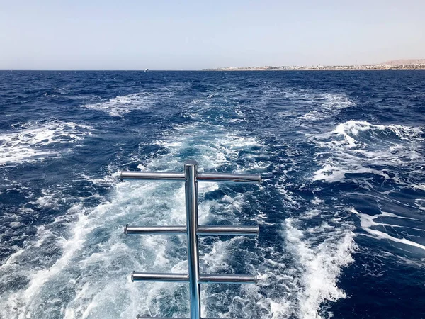 Krom kaplama metal parlak merdiven iniş suya karşı içten içe kaynıyordu arka plan mavi deniz suyu ile dalgalar, bubbles, köpük, yüzme için hızlı bir kayan sepeti sonra tekne izleri.