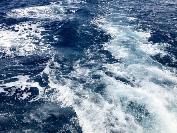 İçten içe kaynıyordu mavi doku deniz tuzlu su dalgalar, dökülmeleri, bubbles, köpük, izleri ile patlamaları sonra hızlı bir kayan sepeti, mavi gökyüzü karşı bir tekne.