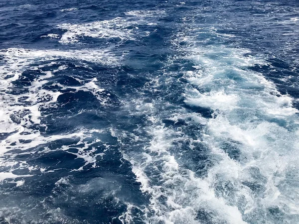 İçten içe kaynıyordu mavi doku deniz tuzlu su dalgalar, dökülmeleri, bubbles, köpük, izler sonra hızlı bir kayan sepeti, mavi gökyüzü karşı bir tekne.