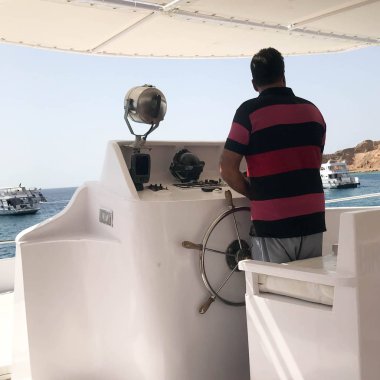 Eski esmer Arap Müslüman geminin kaptanı kırmızı çizgili gömlekli Tamam, bir tekne, bir cruise gemisi denizde, sıcak bir tropikal tatil dönemim duran bir gemiyi kontrol ediyor..
