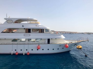 Büyük bir beyaz üç katlı tekne, bir gemi, bir cruise liner hayat şamandıralar, kabinlerin tropikal bir sıcak Güney resort karşı mavi tuz-mavi deniz, okyanus mavi gökyüzü ile.