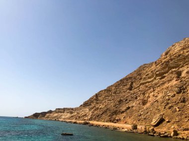 Büyük bir güzel görkemli taş kumlu dağ, bir höyük, bir tepe, mavi gökyüzü ve tuz mavi turkuaz suları ve deniz karşı çölde bir tepe. Manzara.