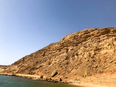 Büyük bir güzel görkemli taş kumlu dağ, bir höyük, bir tepe, mavi bir gökyüzüne karşı çölde bir tepe ve tuz mavisi su ve deniz. Manzara.