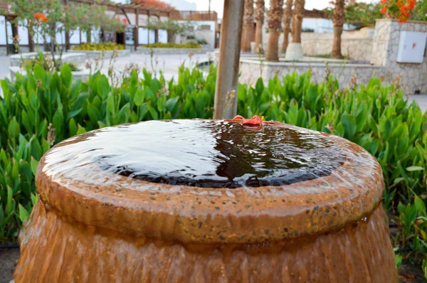 Una bella fontana a forma di vaso marrone, una brocca con gocce d'acqua cadenti su pietre colorate in piedi — Foto Stock