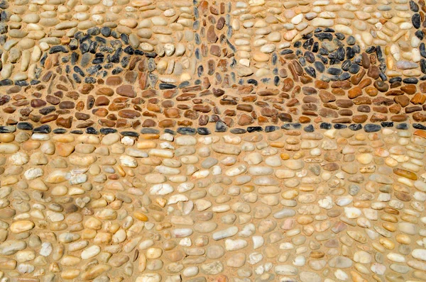 De textuur van de stenen muur, de weg van kleine ronde en ovale stenen met abstracte lijnen aangelegd patronen van zandstrand naden van natuurlijke oude geel zwart bruin. De achtergrond — Stockfoto