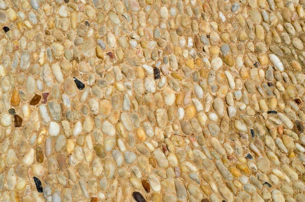 Texture of a stone wall, roads from small round and oval stones with sand with seams of natural old yellow black brown. The background — Stock Photo, Image