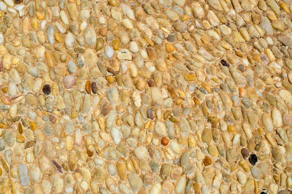 Texture of a stone wall, roads from small round and oval stones with sand with seams of natural old yellow black brown. The background — Stock Photo, Image