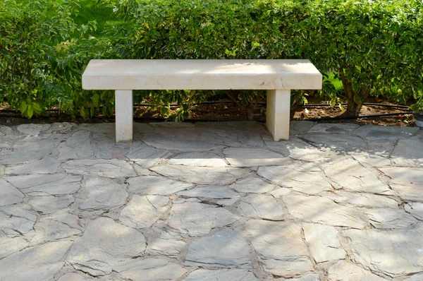 Un banco blanco de piedra sin respaldo en el parque para descansar en un semicamino de piedra sobre el fondo de arbustos verdes — Foto de Stock