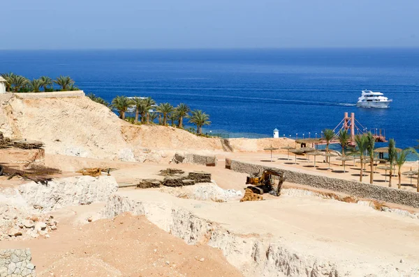 Bouw van een hotel in de woestijn op een warme tropische zuidelijke exotische vakantieresort tegen een blauwe zee met palmbomen en witte schepen — Stockfoto