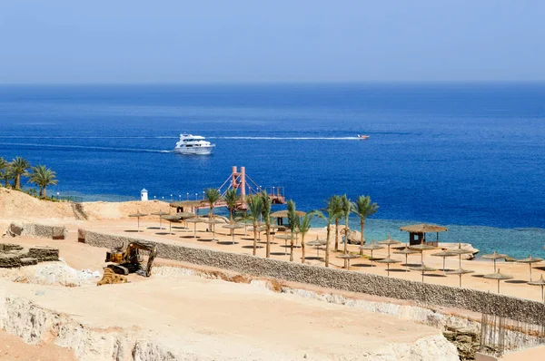 Bouw van een hotel in de woestijn op een warme tropische zuidelijke exotische vakantieresort tegen een blauwe zee met palmbomen en witte schepen — Stockfoto