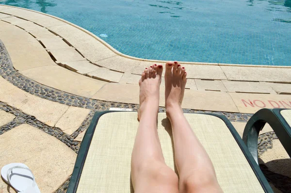 Vackra ben, flickor fötter, kvinnor med rött manikyr på bakgrund av en solstol och pool på en tropisk varm exotisk badort, sommarsemester — Stockfoto