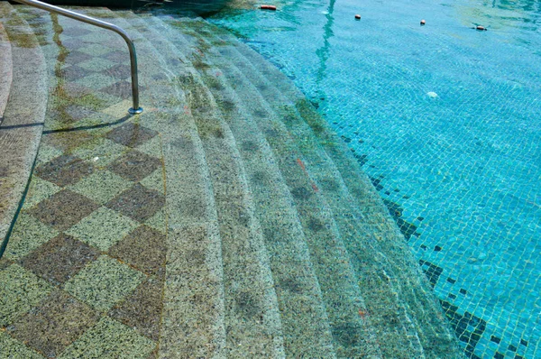 De textuur van de ingang van de afdaling in het zwembad met blauwe water en vierkant keramische tegels op de trappen. De achtergrond — Stockfoto