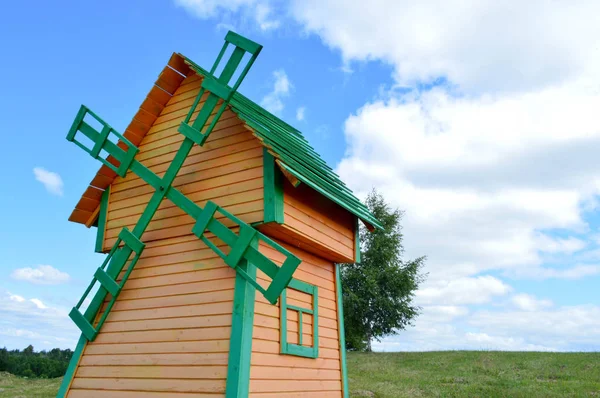 Een mooie houten molen is een rustieke natuurlijke windmolen gemaakt van planken van gele en groene logs tegen een blauwe hemel met wolken — Stockfoto