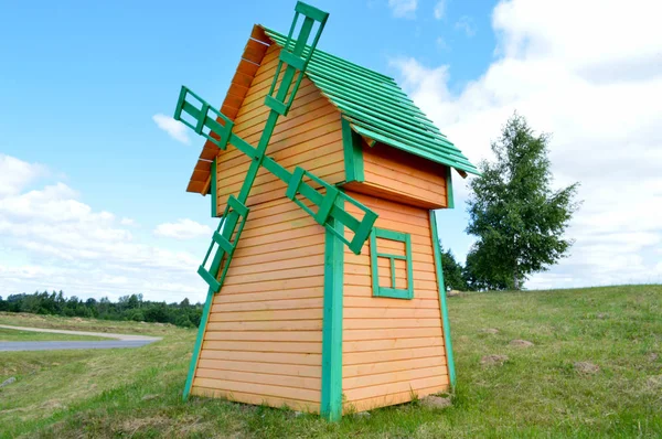 Een mooie houten molen is een rustieke natuurlijke windmolen gemaakt van planken van gele en groene logs tegen een blauwe hemel met wolken — Stockfoto