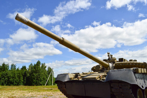 A large green military metal armored deadly dangerous iron Russian Syrian battle tank with a gun turret and a goose is parked parked against a blue sky and clouds outside the city