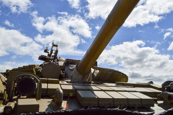 A large green military metal armored deadly dangerous iron Russian Syrian battle tank with a gun turret and a goose is parked parked against a blue sky and clouds outside the city