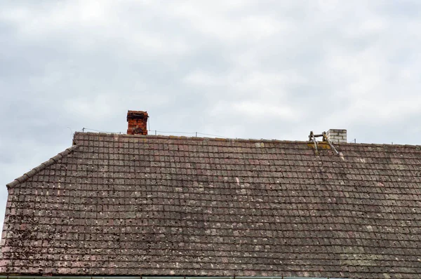 O antigo telhado triangular inclinado da casa, a casa está suja com presas cobertas de musgo contra o céu azul — Fotografia de Stock