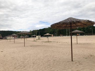 Kötü havalarda boş bir ıssız plaj, mavi gökyüzüne karşı sazdan güneş şemsiyeleri ile off-sezon soğuk sonbahar