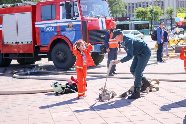 Un pompier apprend à une petite fille en costume coupe-feu ornery à courir avec des tuyaux pour éteindre les pores Biélorussie, Minsk, 08.08.2018 — Photo