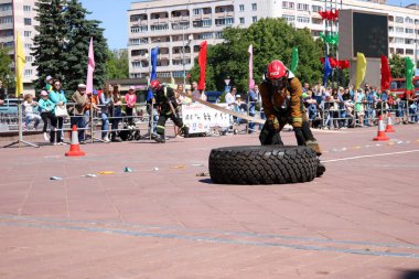 Bir itfaiyeci yanmaz elbise giyip kask içinde çalışır ve rekabet, Belarus, Minsk, 08.08.2018 mücadele yangında büyük lastik tekerlek dönüyor