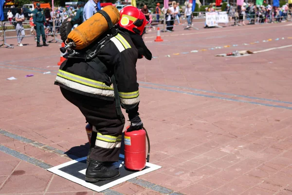 Пожежник у вогнетривкому костюмі і шолом біжить з червоними вогнегасниками, щоб загасити вогонь — стокове фото