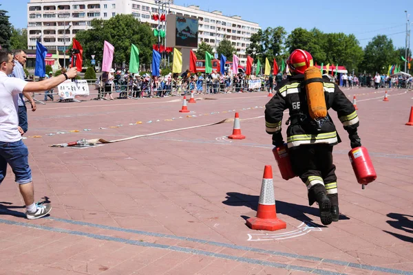 Un bombero con un traje ignífugo y un casco con extintores rojos para extinguir un incendio en una competición de deportes de fuego, Belarús, Minsk, 08.08.2018 — Foto de Stock