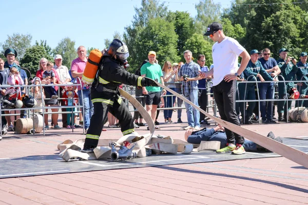 A fireman in a fireproof suit and a helmet running with an oxygen balloon pulling, holding a fire hose at a fire sport competition. Minsk, Belarus, 08.07.2018 — Stock Photo, Image