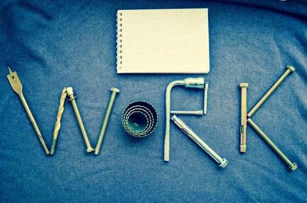 Die Aufschrift "Arbeit" wird von den metallischen Ankerbolzen, den Schrauben, swermami, den Schlüsseln geschrieben. "Arbeit" aus Objekten. Textarbeit aus einem Metallwerkzeug und Notizblock — Stockfoto