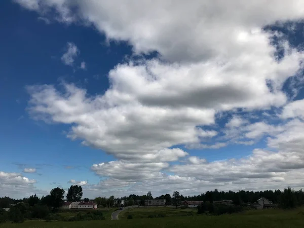 Krásné modré nebe s bílými nadýchanými mraky pozadí zelené trávy a vesnických staveb. Na pozadí — Stock fotografie
