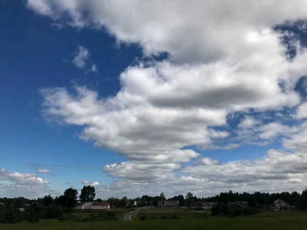 Ein schöner blauer Himmel mit weißen, flauschigen Wolken vor dem Hintergrund von Dorfgebäuden und grünem Gras. der Hintergrund — Stockfoto