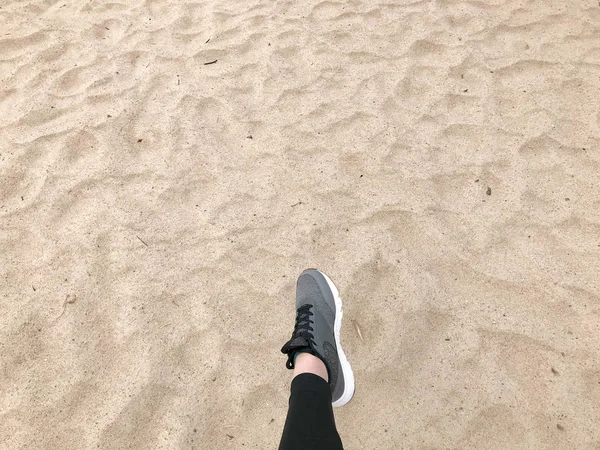 Το πόδι στο παπούτσι γκρι εκκίνησης κάνει ένα βήμα στο πλαίσιο της ένα φυσικό χαλαρά Κίτρινο χρυσό όμορφη ζεστή άμμο παραλιών — Φωτογραφία Αρχείου