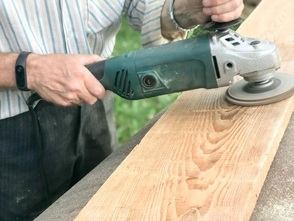 Muž pracuje rukama, brousí disk kolem pro brusku, elektrický nástroj pro broušení a leštění povrchu dřevěné desky — Stock fotografie