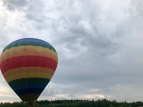 Grand ballon volant rayé multicolore lumineux rond rayé arc-en-ciel avec un panier contre le ciel dans la soirée — Photo