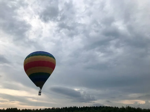 Grand ballon volant rayé multicolore lumineux rond rayé arc-en-ciel avec un panier contre le ciel dans la soirée — Photo
