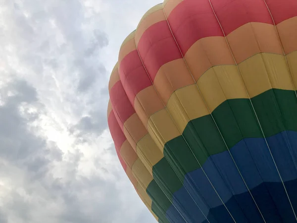 Grote multi-gekleurde lichte ronde regenboog gekleurde gestreepte gestreepte vliegende ballon met een mandje tegen de hemel in de avond — Stockfoto