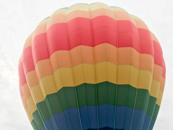 Large multi-colored bright round rainbow colored striped striped flying balloon with a basket against the sky in the evening — Stock Photo, Image