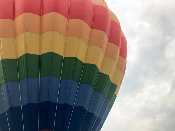 Grote multi-gekleurde lichte ronde regenboog gekleurde gestreepte gestreepte vliegende ballon met een mandje tegen de hemel in de avond — Stockfoto