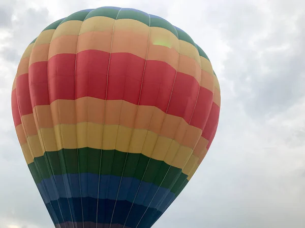 Grande arco-íris redondo brilhante multicolorido colorido listrado balão voador com uma cesta contra o céu à noite — Fotografia de Stock