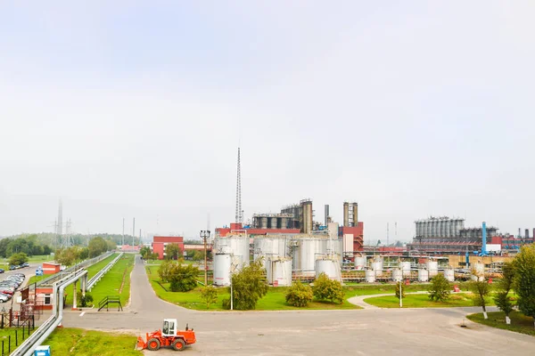 Industrial landscape with chemical plants, pipes and columns. Below is an orange tractor. Smoke comes from the reactor. Panoramic view of repair production. Process pipes