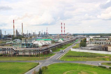 Endüstriyel manzara. Panoramik teknolojik borular. Fabrika ayarları. Kimyasal kırmızı-beyaz borulardan duman geliyor. Üretim binalar. Gökyüzü ve parlak çim arka planı