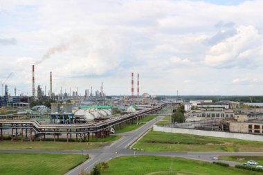 Endüstriyel manzara. Panoramik teknolojik borular. Fabrika ayarları. Kimyasal kırmızı-beyaz borulardan duman geliyor. Üretim binalar. Gökyüzü ve parlak çim arka planı