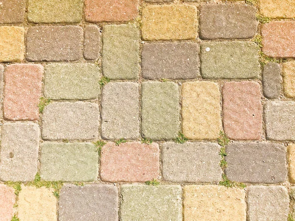 Textura de multicoloridas belas pedras retangulares concreto pavimentação telhas de tijolo com costuras cobertas com grama verde. O fundo — Fotografia de Stock